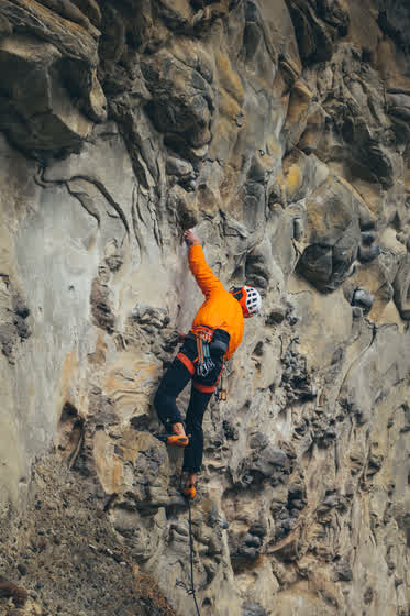 Escaladora de naranja sobre la pared llena de cantos rodados