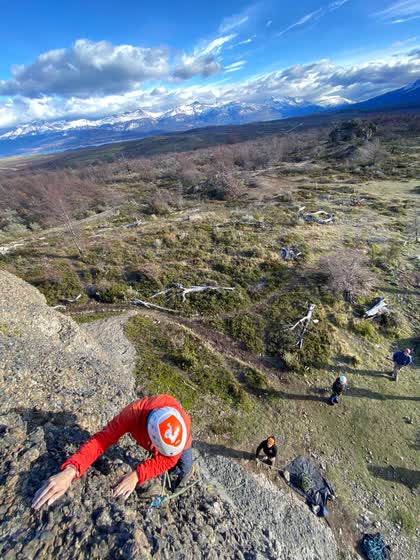 Escalador de rojo saliendo por arriba, con el grupo abajo y el lago y las montañas nevadas al fondo