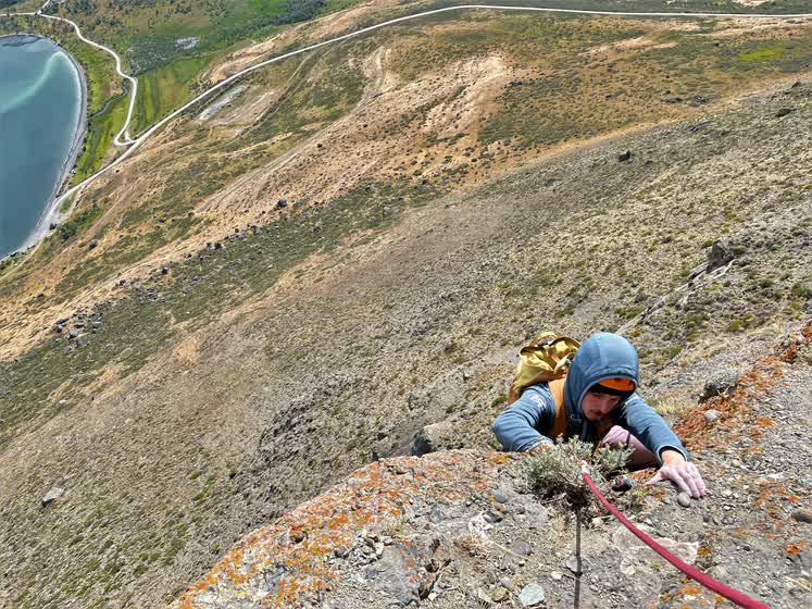 Escalador saliendo por arriba sobre la roca cubierta de líquenes, con el valle abajo
