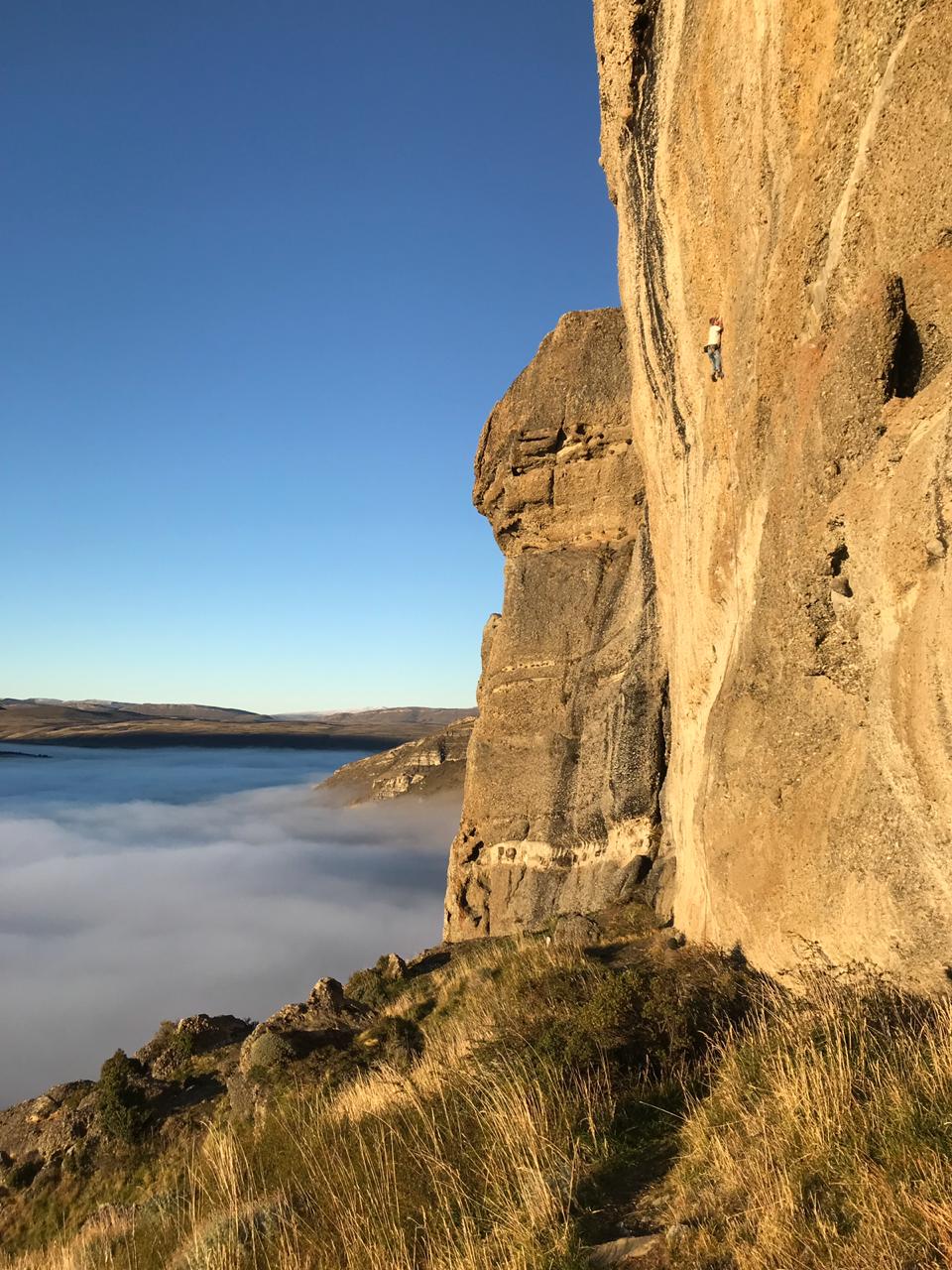 Escalador en la pared vertical de conglomerado del Cerro Benítez, al amanecer, sobre un mar de nubes que cubre el valle