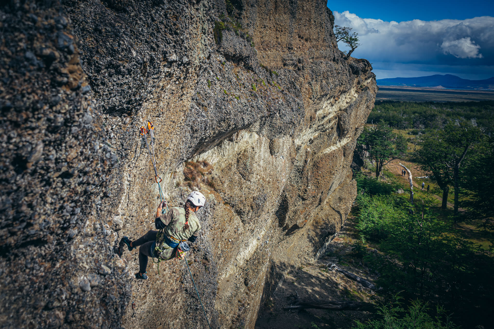 Escaladora descendiendo por la pared de conglomerado del Cerro Benítez, con la estepa y el bosque al fondo