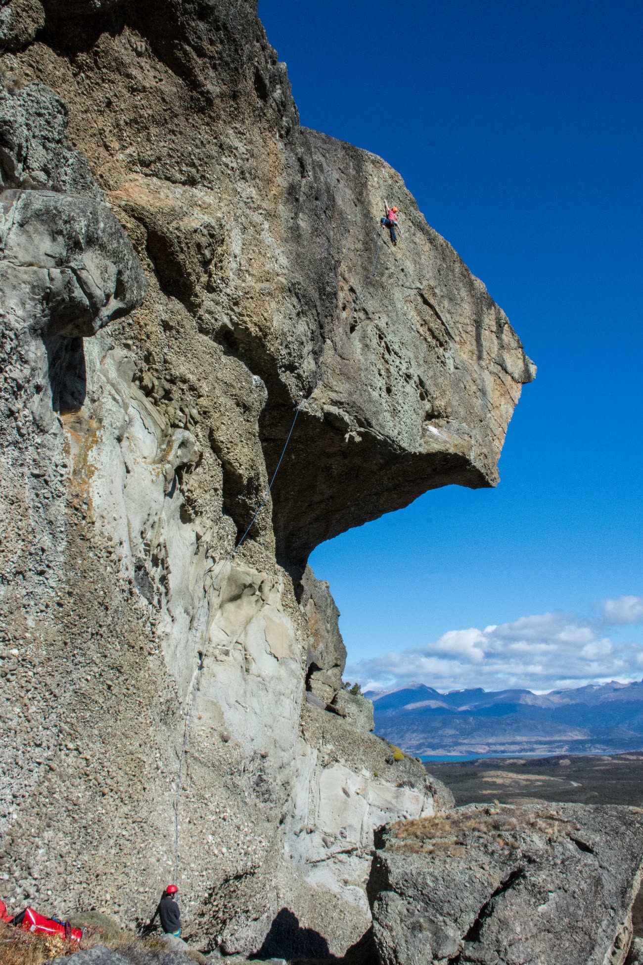 Escalador en el filo de la gran visera de conglomerado del Cerro Benítez, con su asegurador abajo y la estepa patagónica al fondo